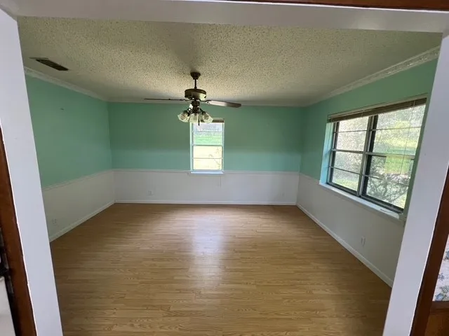 Unfurnished dining area featuring light wood-type flooring, a textured ceiling, ceiling fan, and ornamental molding