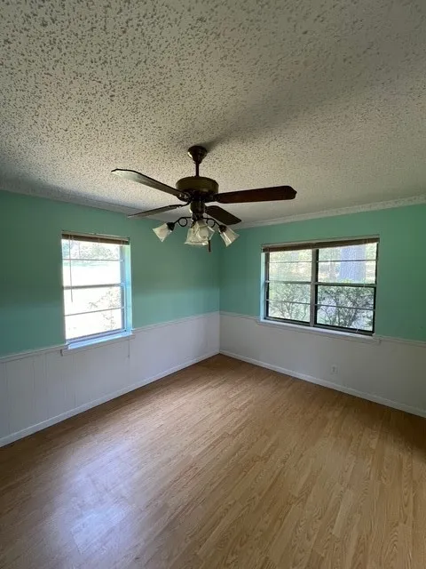 Unfurnished room featuring light wood-style flooring, a textured ceiling, wainscoting, and a ceiling fan