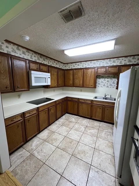 Kitchen featuring light countertops, refrigerator, a textured ceiling, light tile patterned flooring, and wallpapered walls
