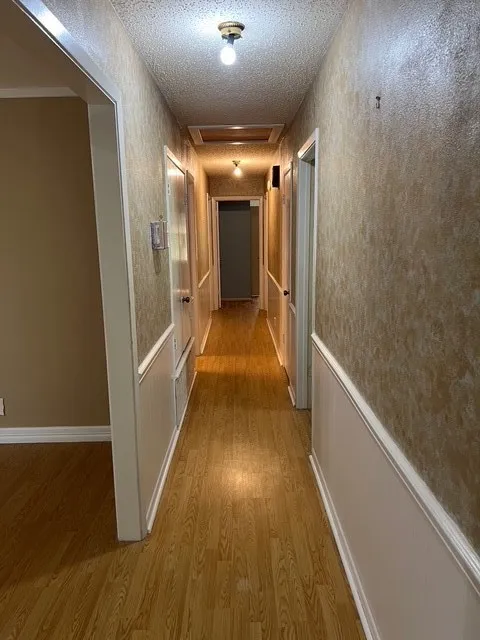 Corridor with light wood finished floors, attic access, and a textured ceiling