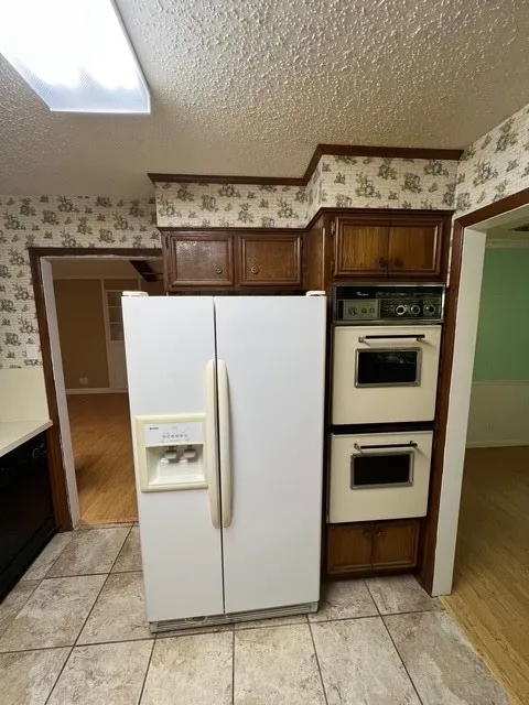 Kitchen featuring white appliances, wallpapered walls, a textured ceiling, dark brown cabinets, and light countertops