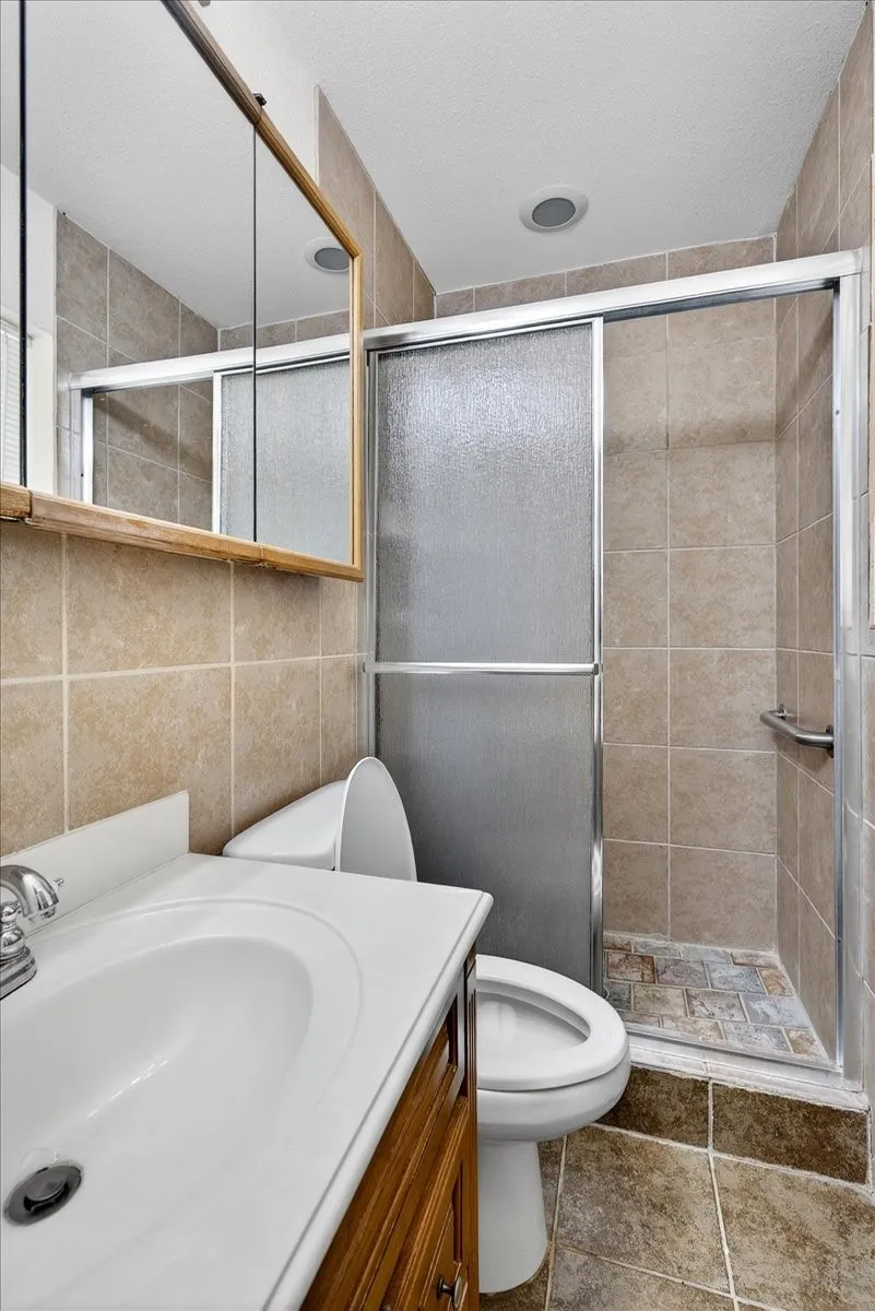 Full bath featuring vanity, a stall shower, tile walls, and tile patterned flooring