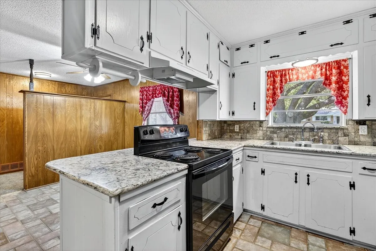 Kitchen with white cabinets, black range with electric stovetop, a textured ceiling, wooden walls, and under cabinet range hood