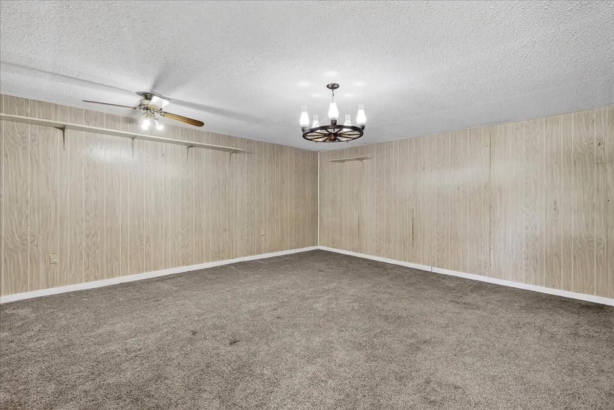 Unfurnished room featuring a chandelier, light carpet, a textured ceiling, and ceiling fan