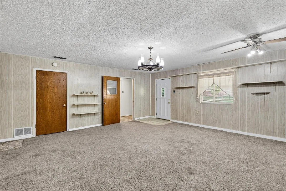 Unfurnished room with a ceiling fan, light colored carpet, a chandelier, a textured ceiling, and wooden walls