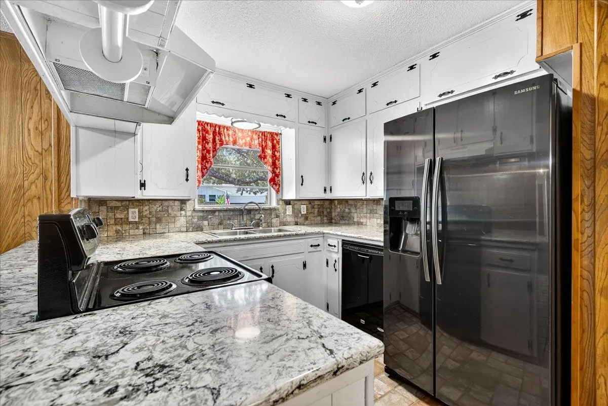 Kitchen with range hood, black appliances, white cabinets, decorative backsplash, and a textured ceiling