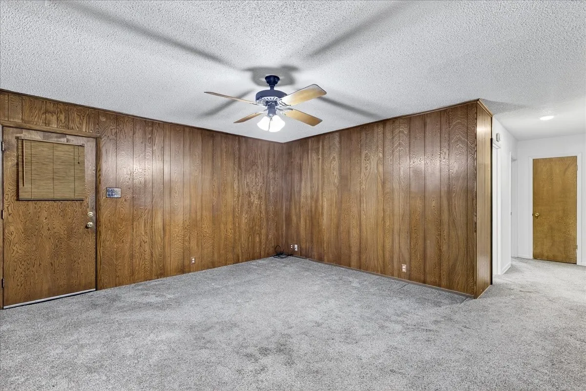 Empty room featuring light carpet, wooden walls, a textured ceiling, and a ceiling fan