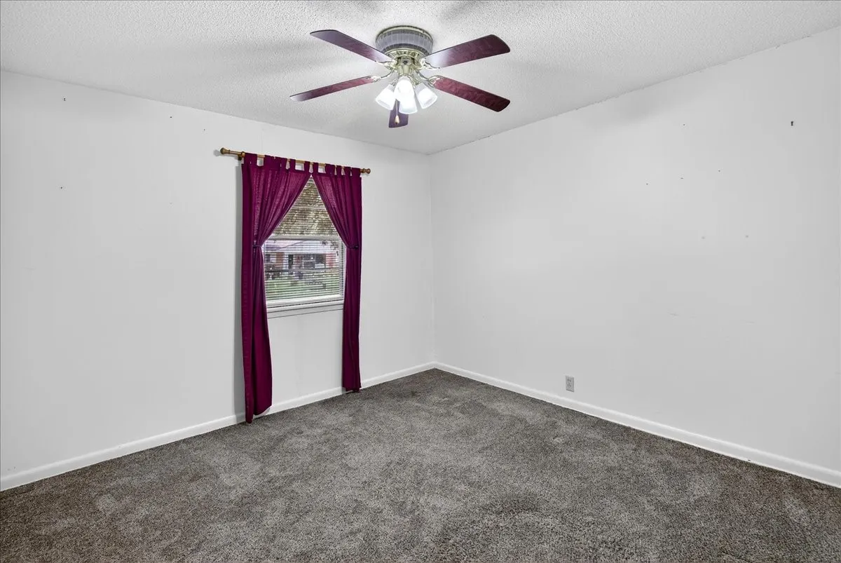 Empty room featuring dark carpet, a textured ceiling, and ceiling fan