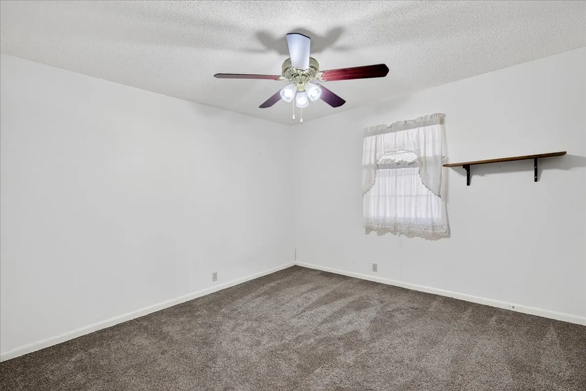 Empty room featuring dark colored carpet, a textured ceiling, and a ceiling fan