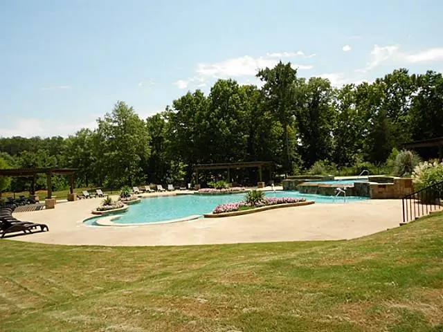 Community pool featuring a patio area, a jacuzzi, a lawn, and view of scattered trees