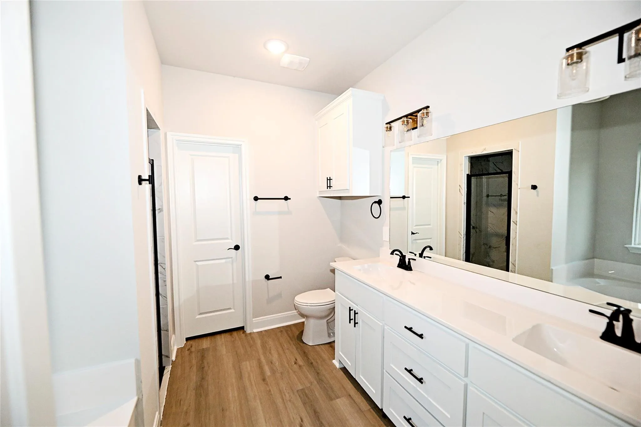 Bathroom featuring wood-type flooring, dual bowl vanity, a bathtub, and toilet