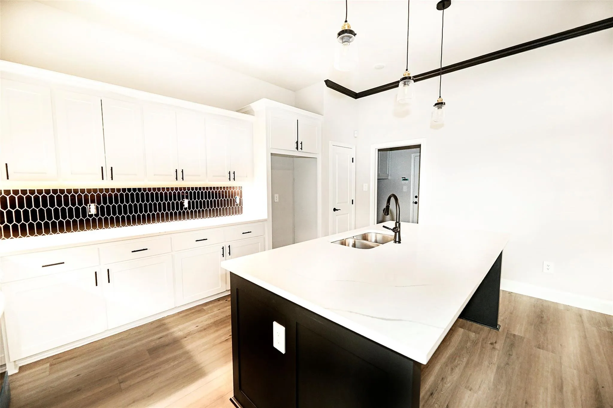Kitchen with decorative backsplash, hanging light fixtures, light wood-type flooring, and sink
