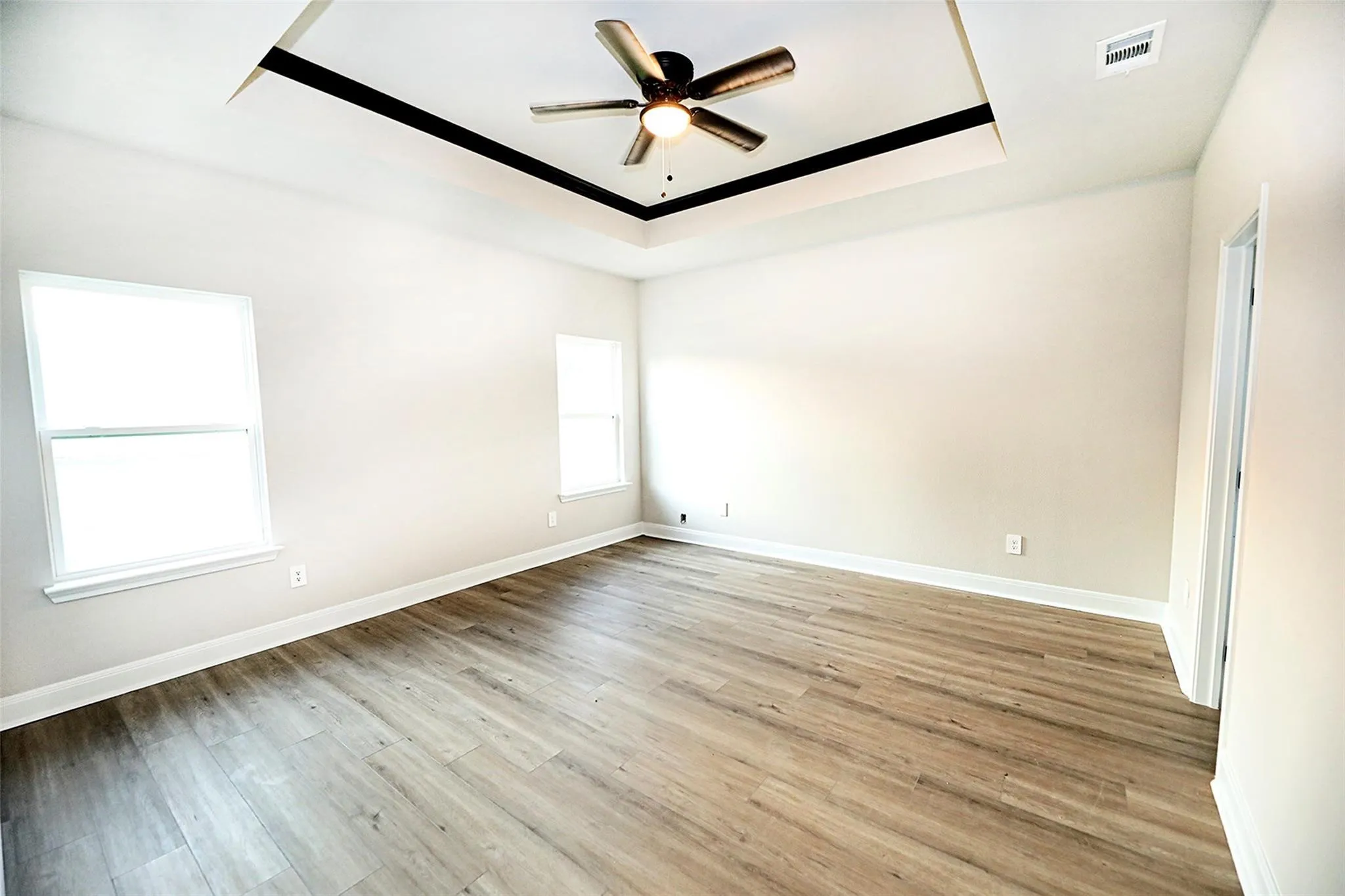 Spare room featuring a tray ceiling, ceiling fan, and light hardwood / wood-style floors