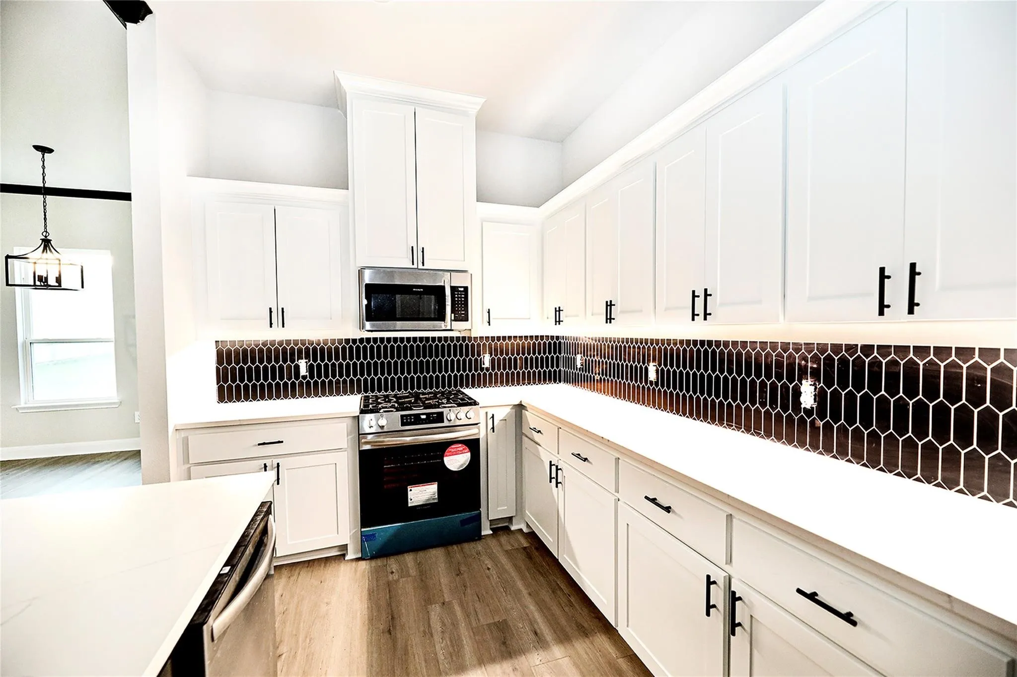 Kitchen with appliances with stainless steel finishes, dark wood-type flooring, white cabinetry, and decorative light fixtures