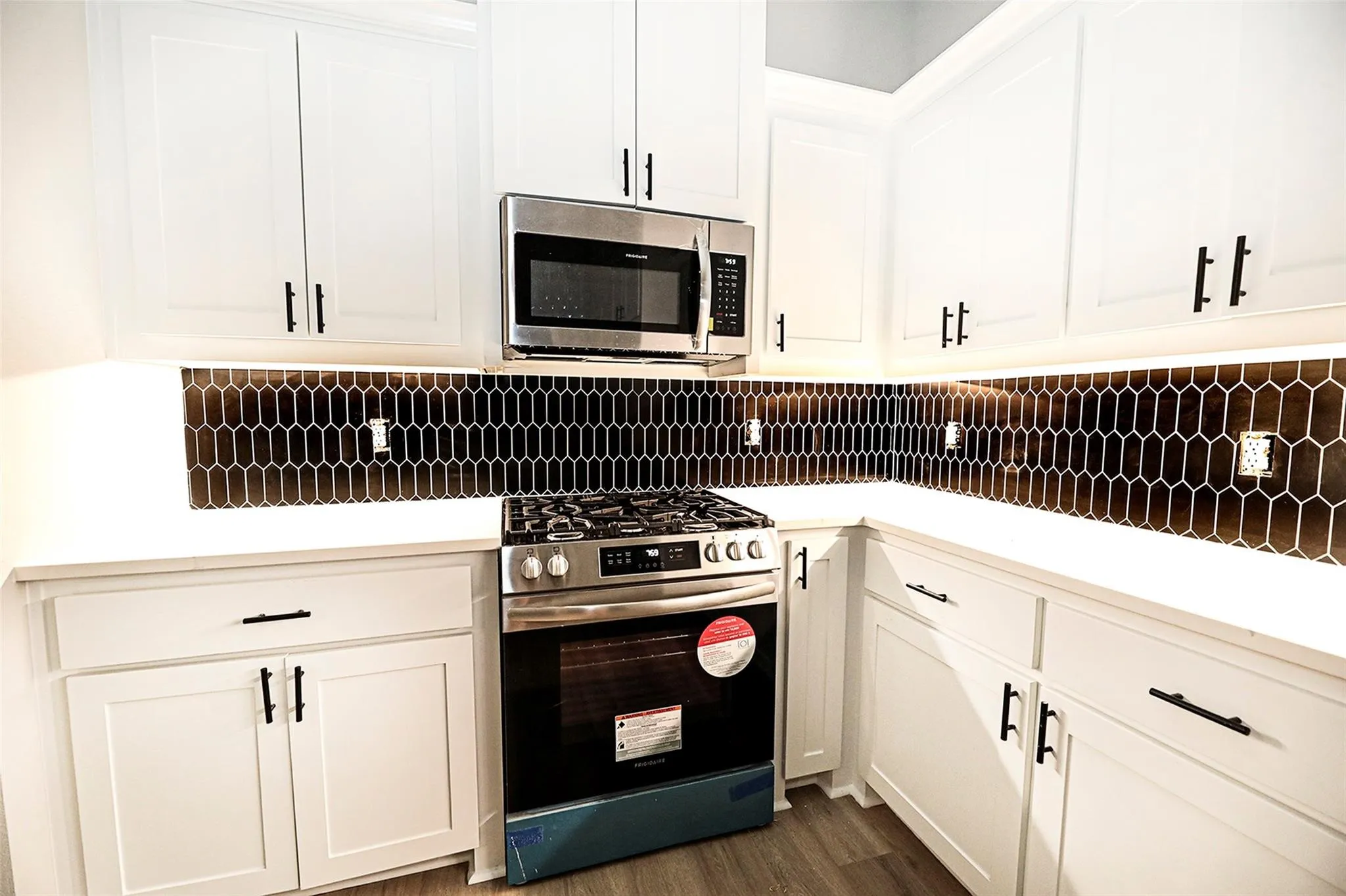 Kitchen featuring appliances with stainless steel finishes, dark wood-type flooring, white cabinets, and backsplash