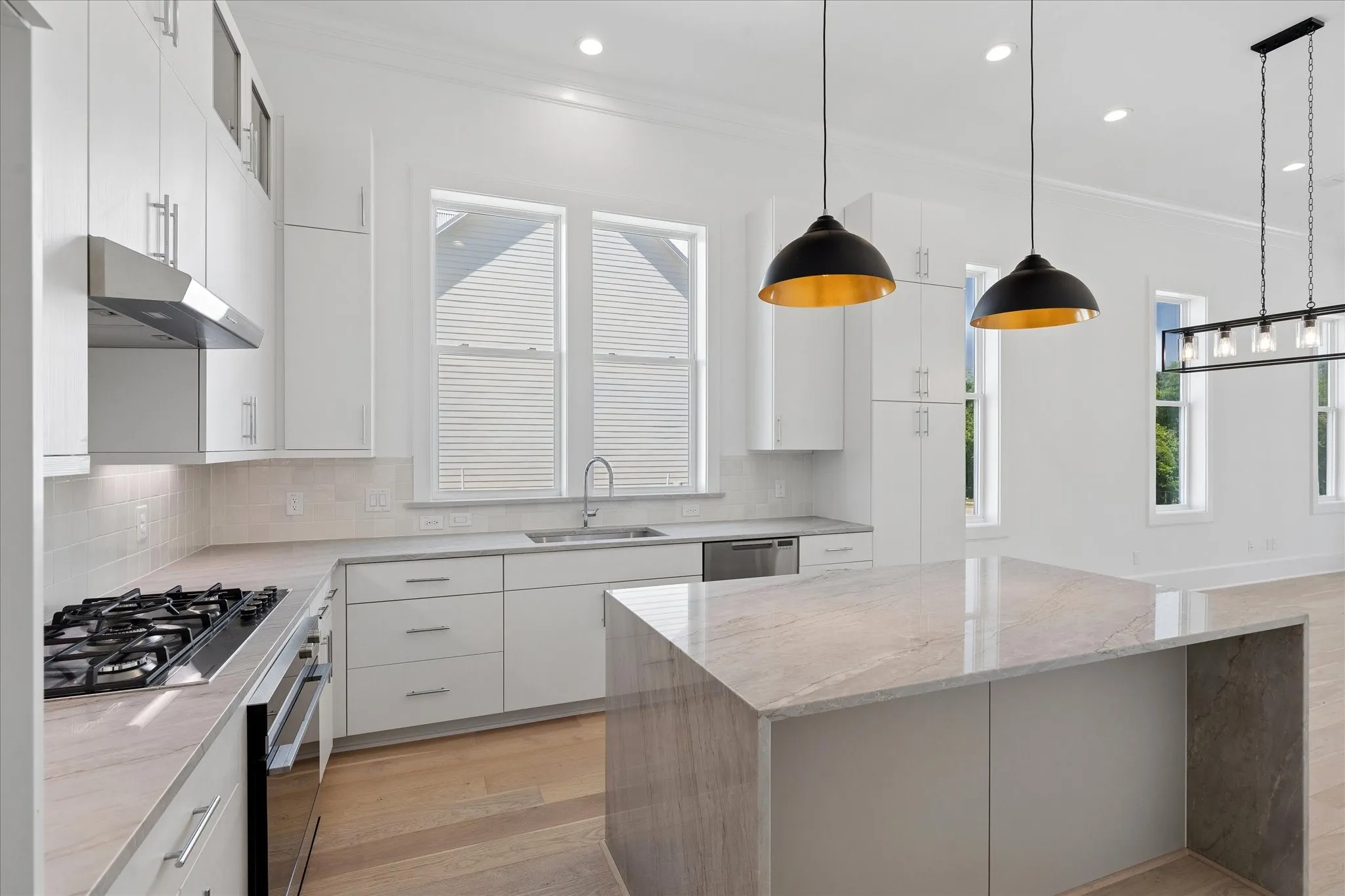Open-concept kitchen featuring an oversized island with stone waterfall countertop, white shaker cabinetry, stainless steel appliances, and recessed lighting