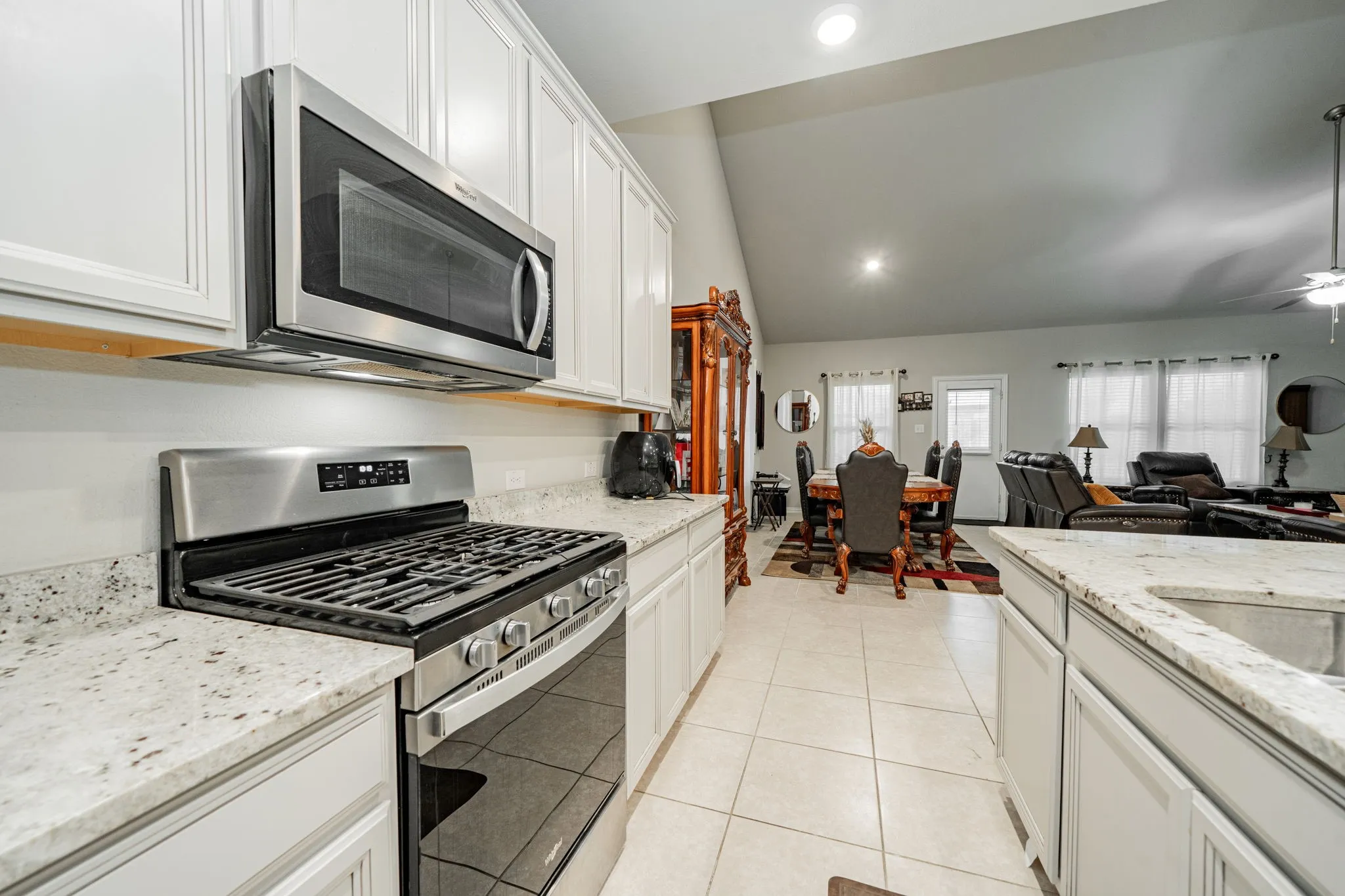 Kitchen featuring stainless steel appliances, light stone countertops, lofted ceiling, white cabinetry, and recessed lighting