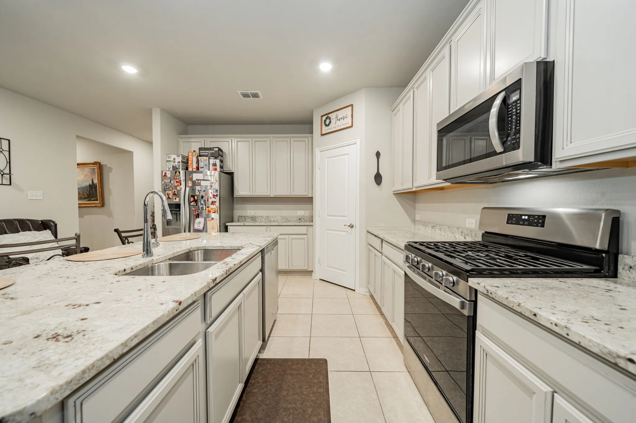 Kitchen with appliances with stainless steel finishes, light tile patterned floors, light stone counters, recessed lighting, and white cabinetry