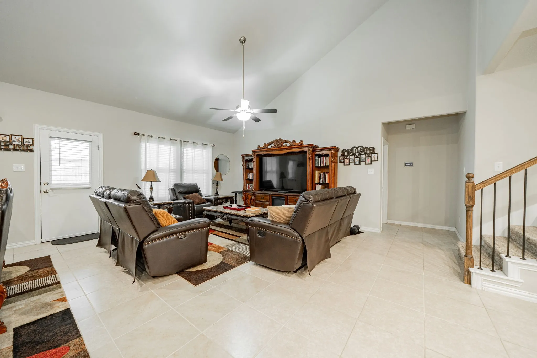 Living room with high vaulted ceiling, ceiling fan, light tile patterned floors, and stairs
