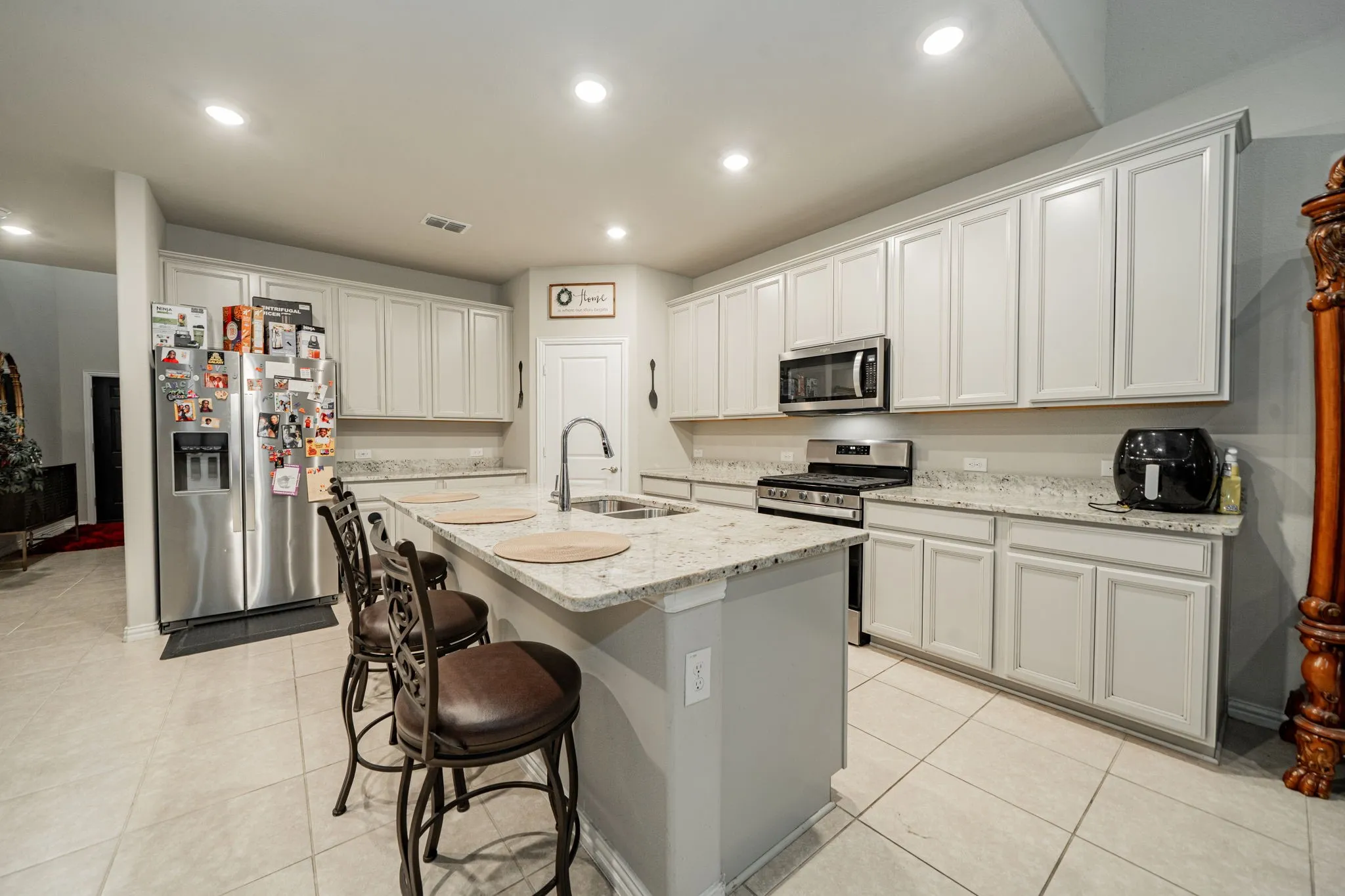 Kitchen featuring light stone counters, stainless steel appliances, a kitchen breakfast bar, recessed lighting, and light tile patterned floors