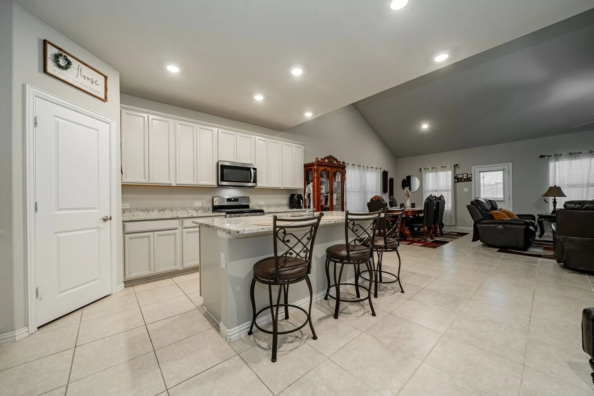 Kitchen with lofted ceiling, open floor plan, a breakfast bar area, an island with sink, and light stone counters