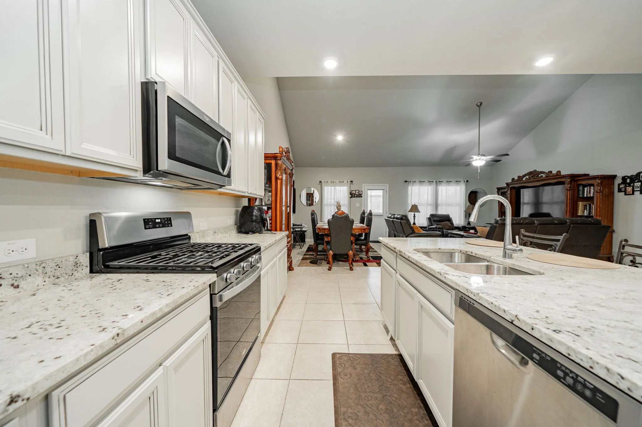Kitchen with stainless steel appliances, light stone counters, recessed lighting, vaulted ceiling, and light tile patterned flooring