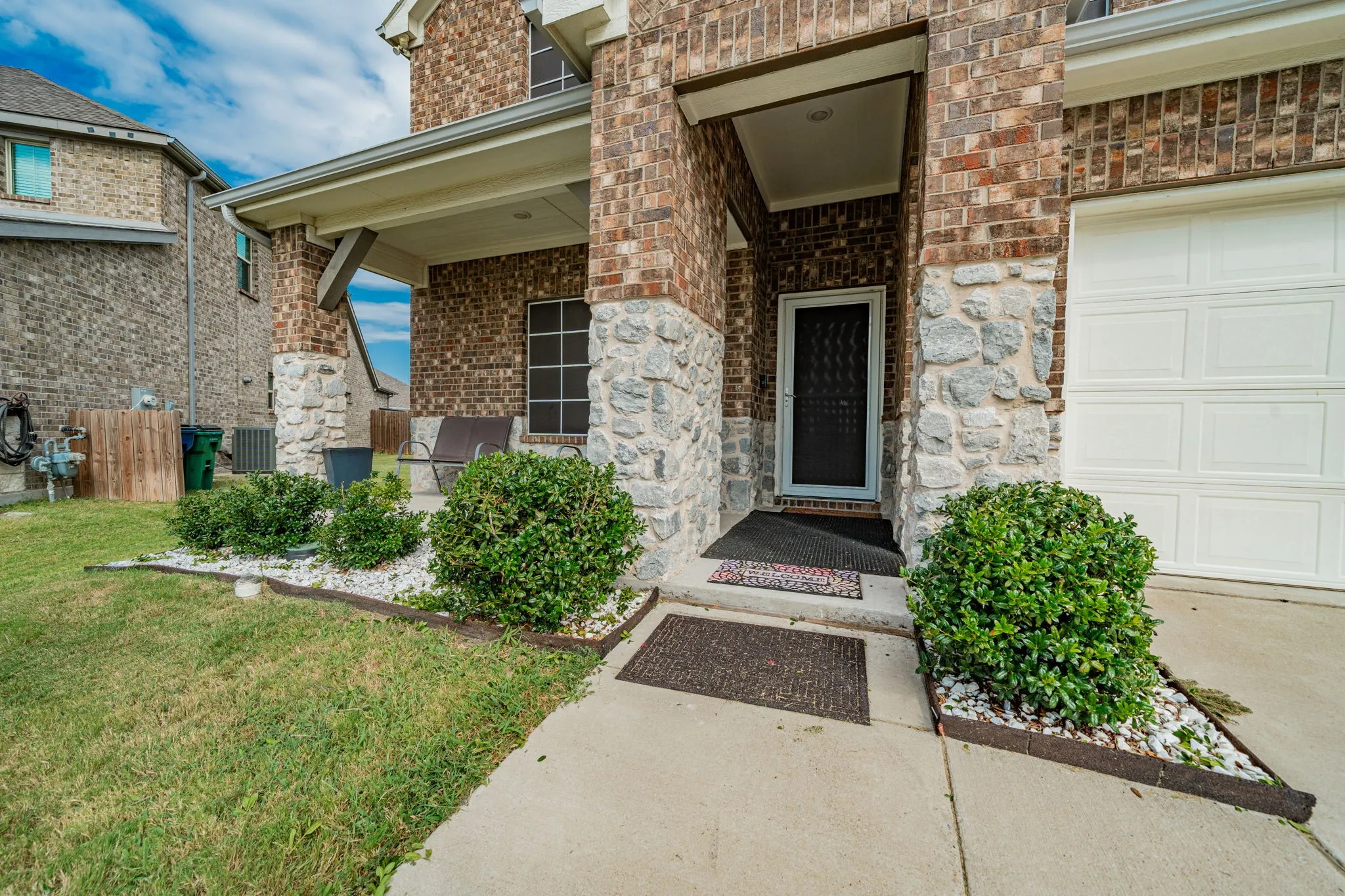 View of exterior entry featuring a porch, stone siding, brick siding, and a garage