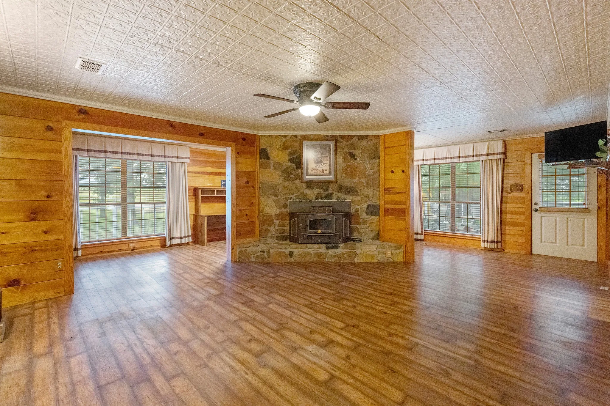 Unfurnished living room featuring wood walls, a wood stove, healthy amount of natural light, an ornate ceiling, and wood finished floors