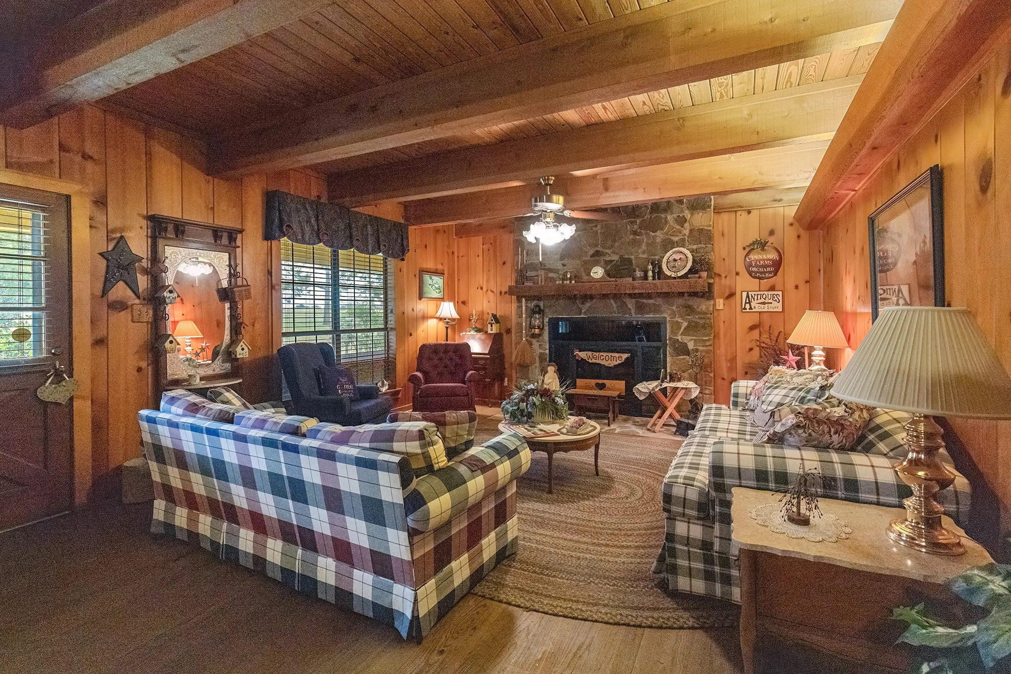 Living area with wood walls, a fireplace, wood finished floors, a ceiling fan, and a wooden ceiling with exposed beams