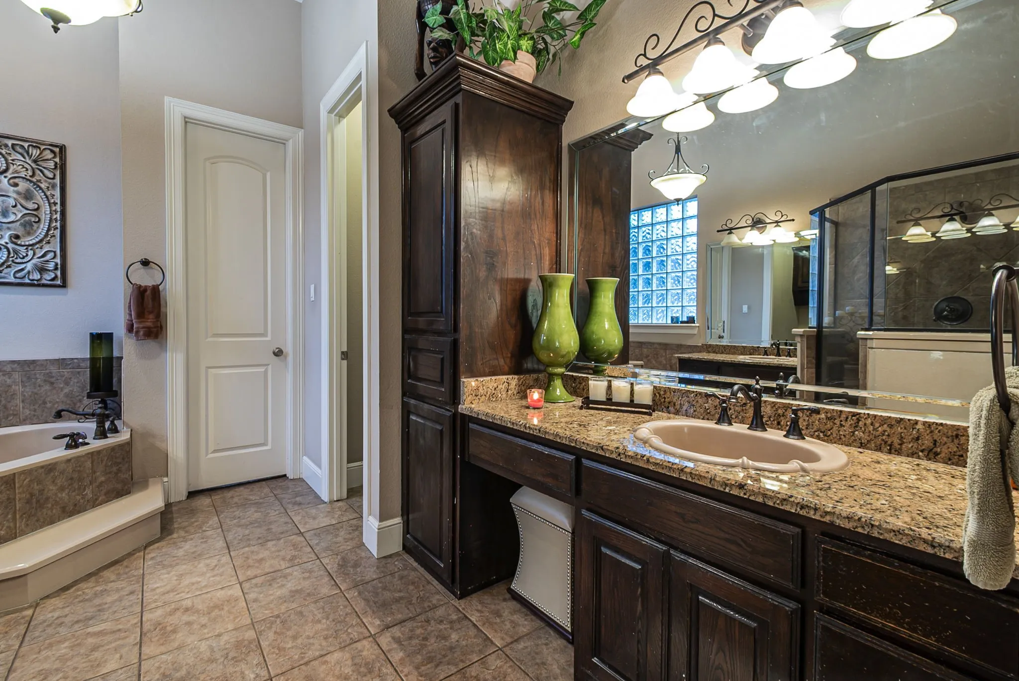 Primary bathroom featuring dual sinks with granite countertops, jetted tub, and beautiful cabinetry.