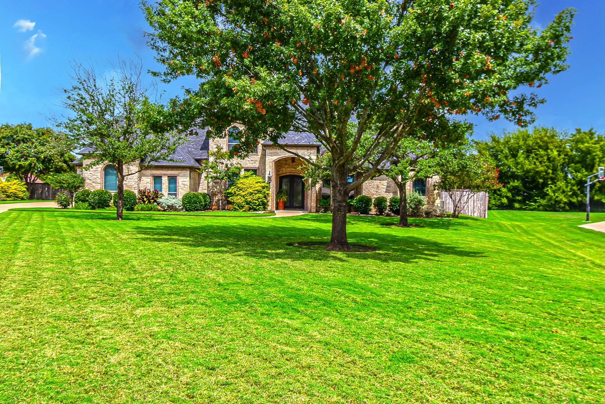 Another view of the home with large yard, mature trees, and beautiful landscaping.