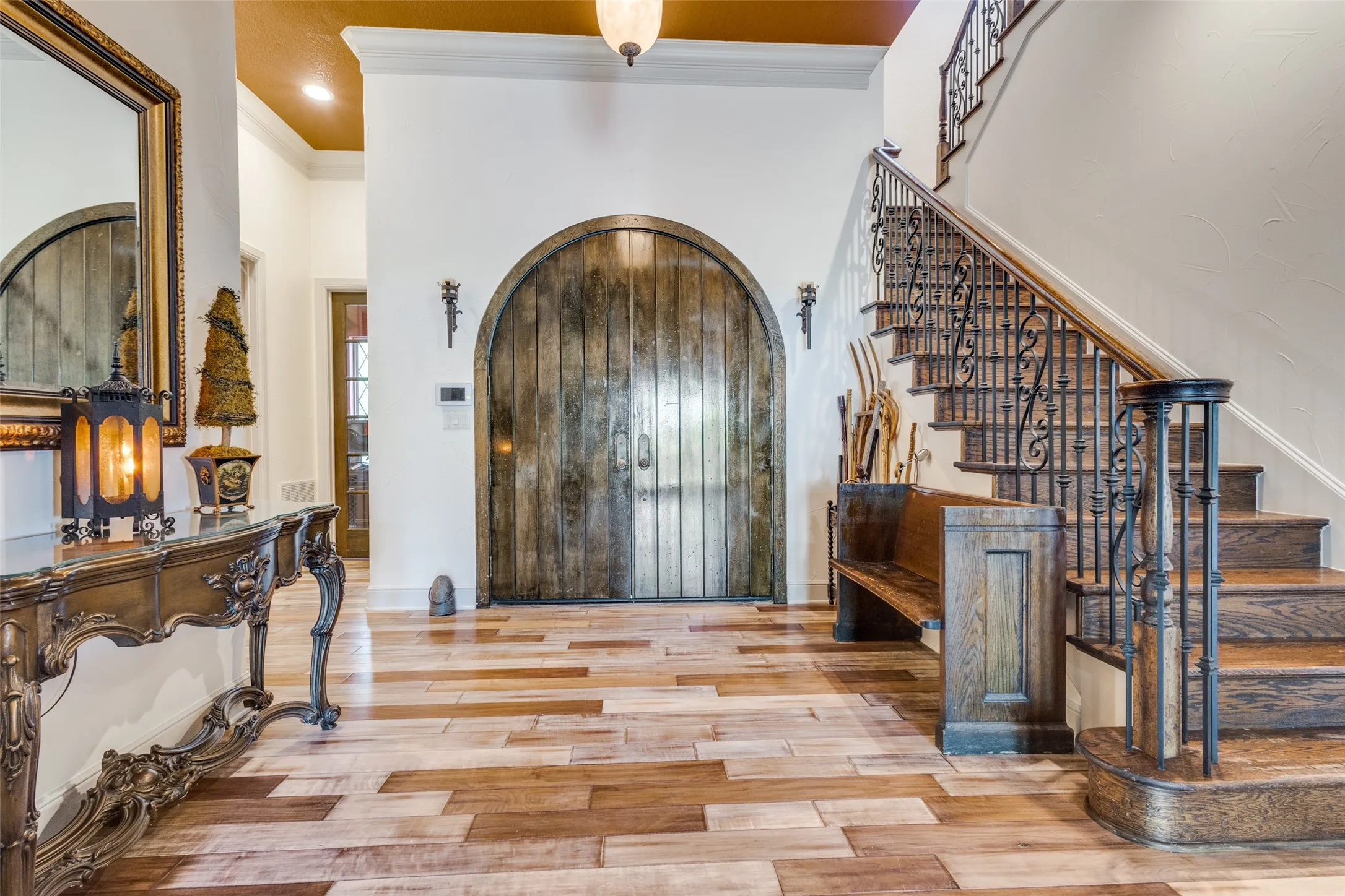 Entrance foyer with crown molding, arched walkways, light wood-style flooring, and a towering ceiling