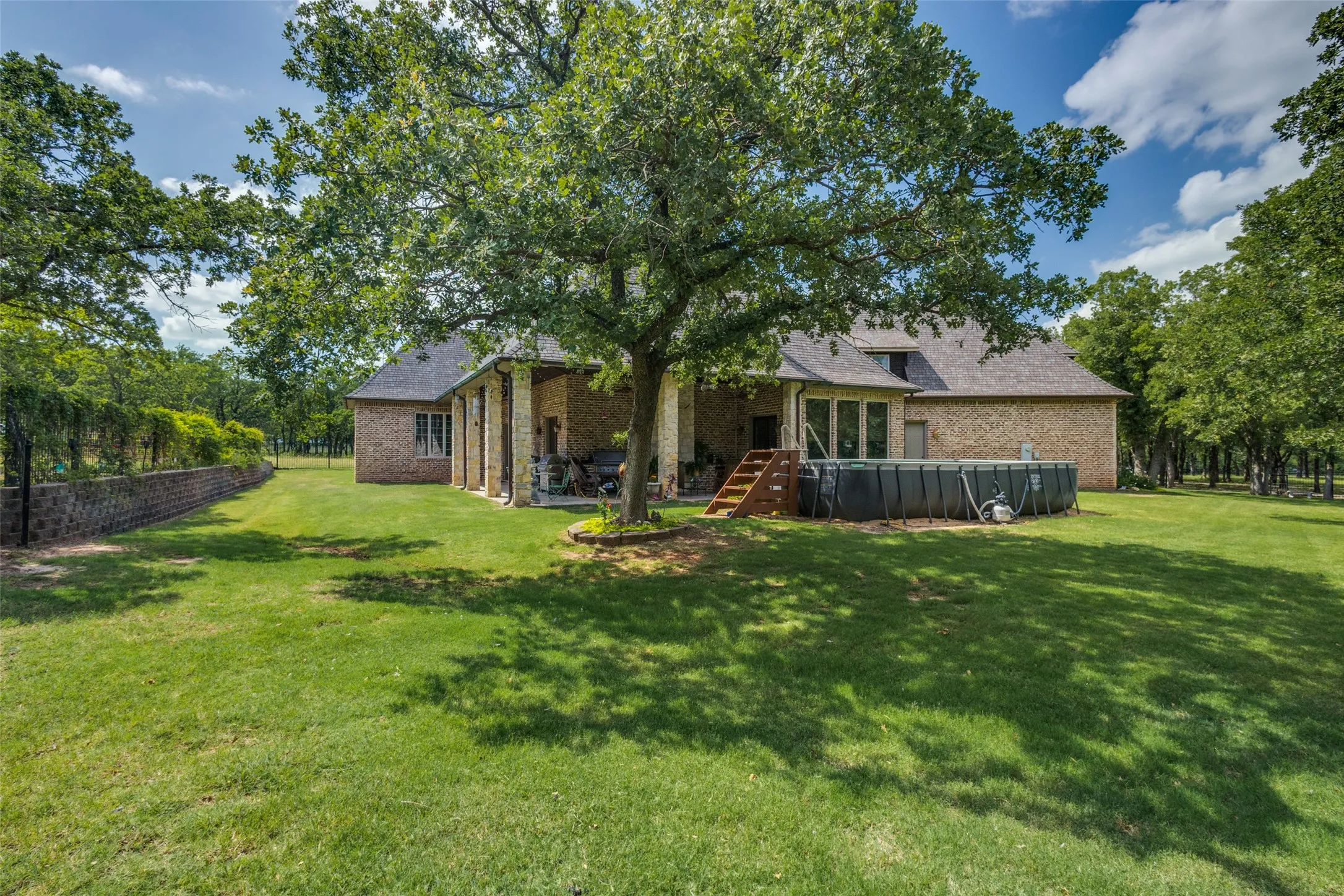 Back of property with brick siding, an outdoor pool, a patio, and roof with shingles