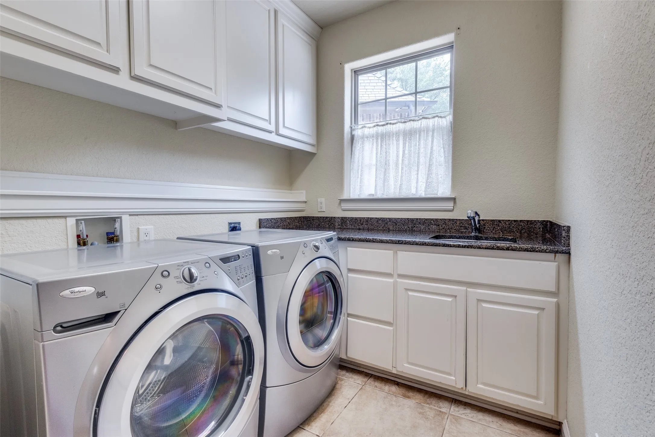 Laundry area featuring a textured wall, cabinet space, light tile patterned flooring, and washer and dryer