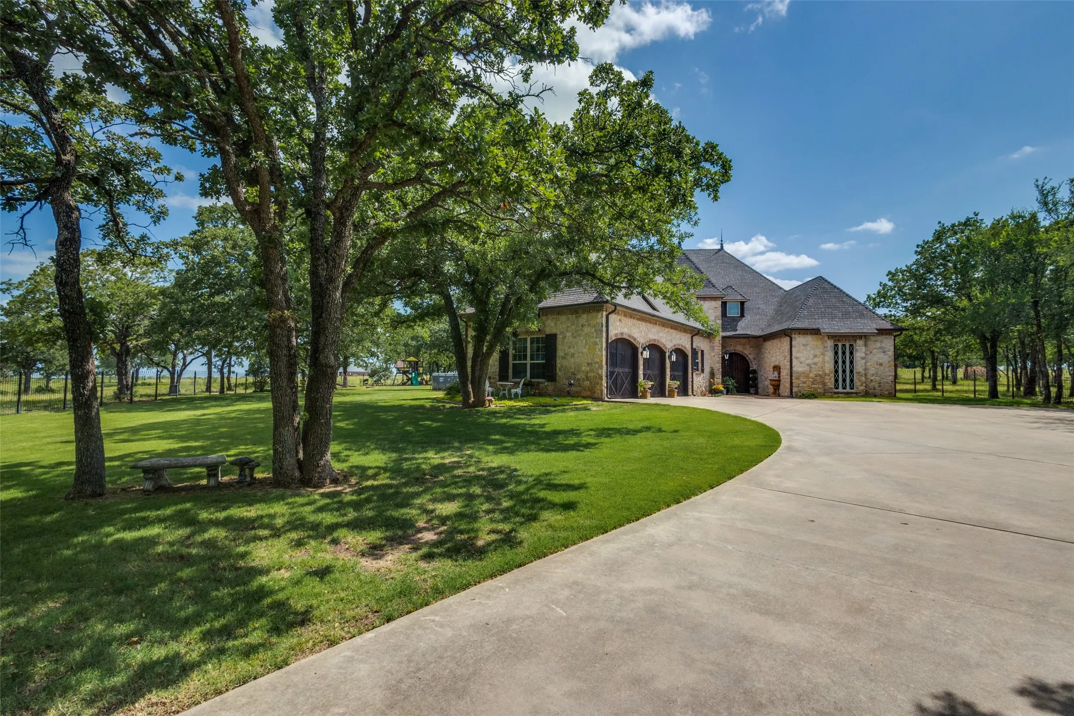 View of front of property featuring stone siding, a front lawn, and curved driveway