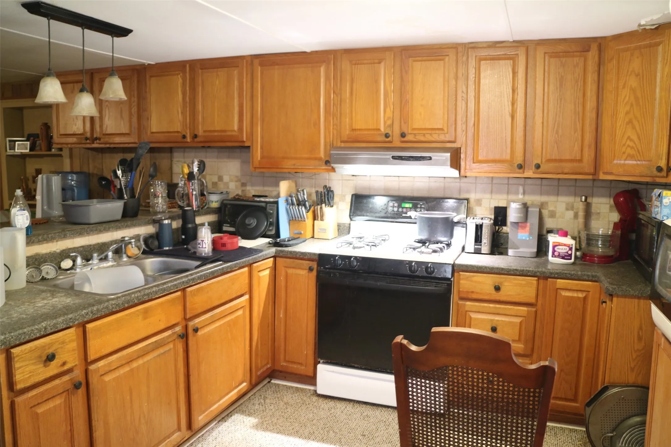 Kitchen featuring range with gas cooktop, backsplash, brown cabinets, and dark countertops