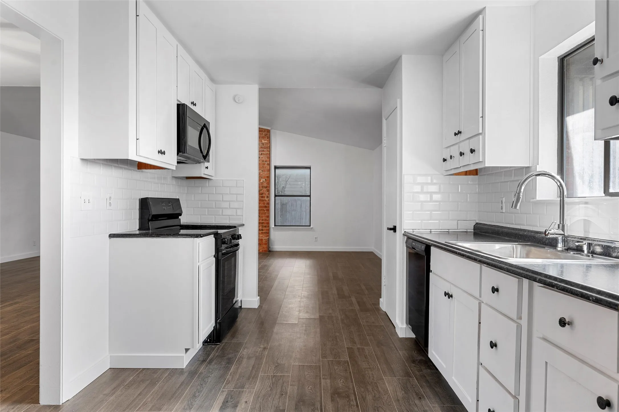Kitchen with backsplash, black appliances, dark wood-style flooring, white cabinetry, and vaulted ceiling