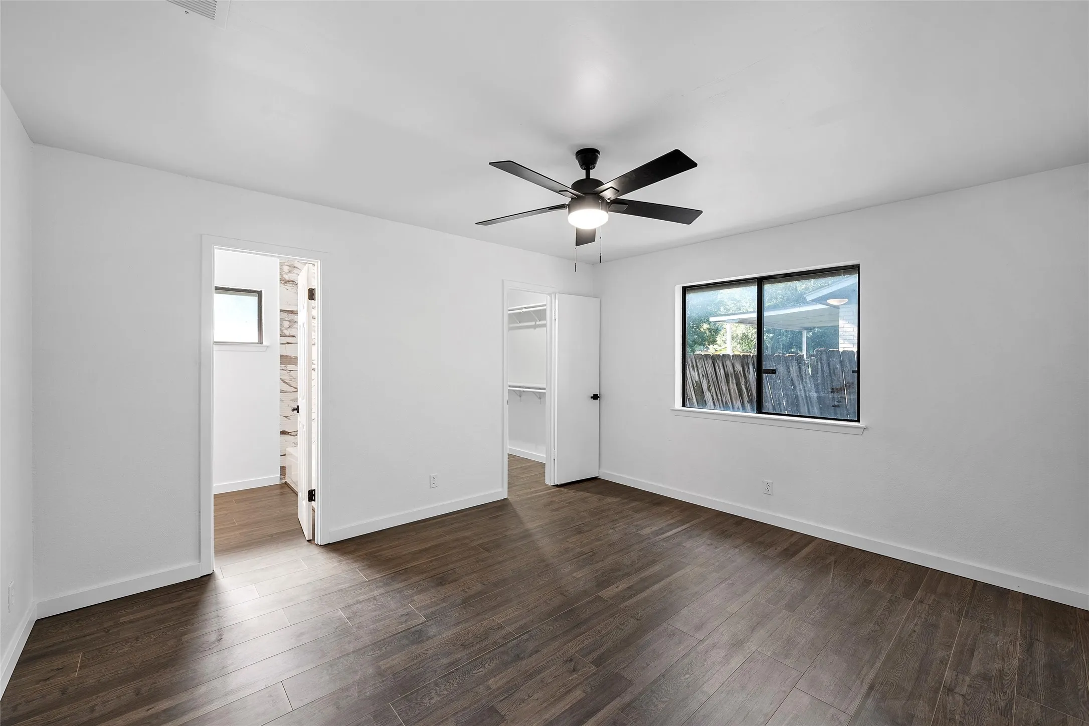 Unfurnished bedroom featuring a spacious closet, dark wood-style floors, and a ceiling fan