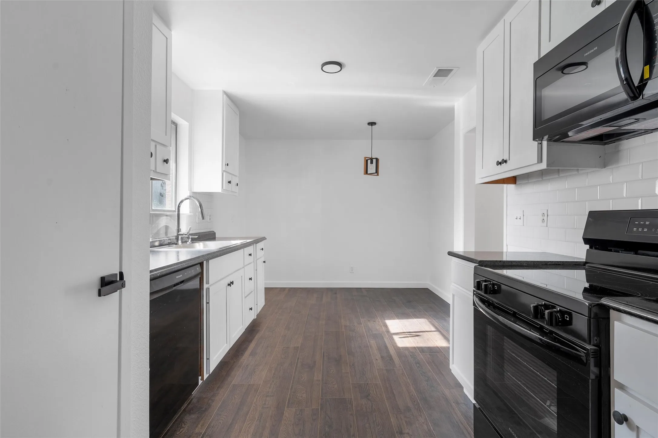 Kitchen with black appliances, white cabinets, decorative backsplash, and decorative light fixtures