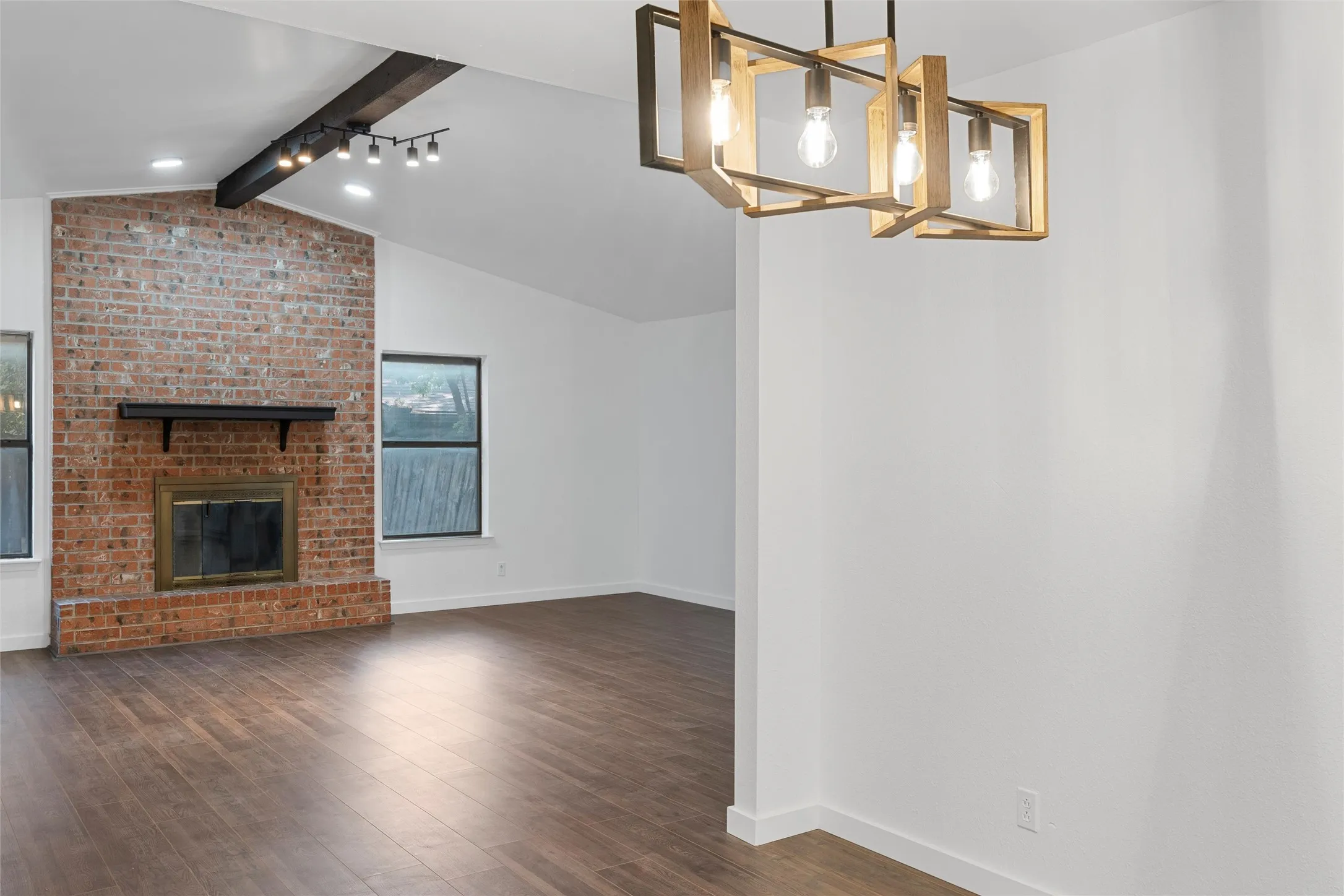 Unfurnished living room with dark wood-style floors, a brick fireplace, and a chandelier