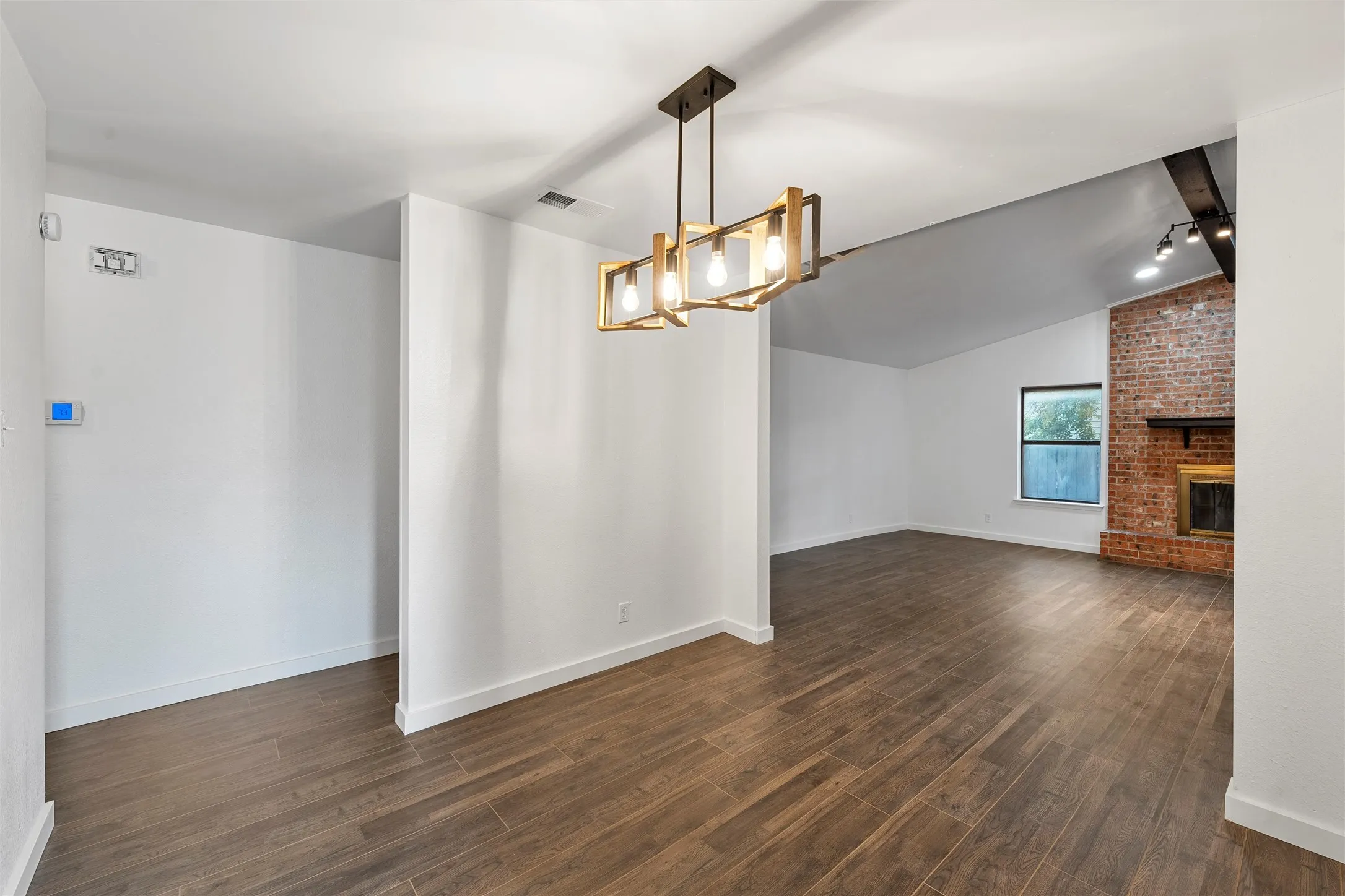 Unfurnished dining area featuring dark wood-type flooring, a brick fireplace, and a chandelier