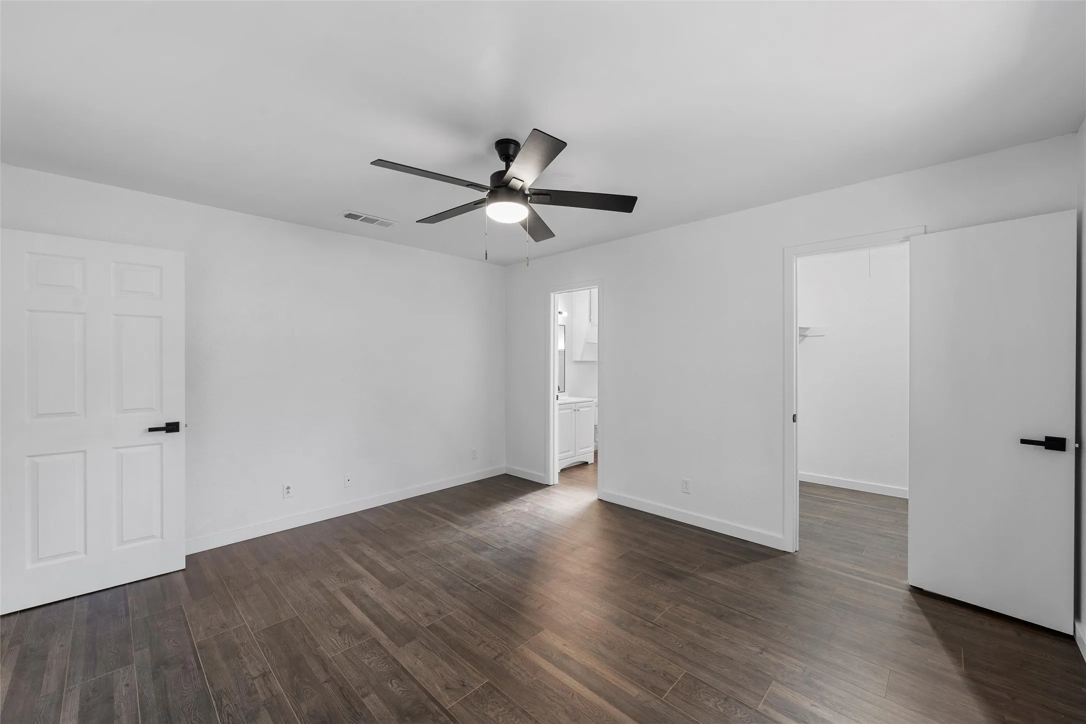 Unfurnished bedroom featuring a spacious closet, dark wood-type flooring, and ceiling fan