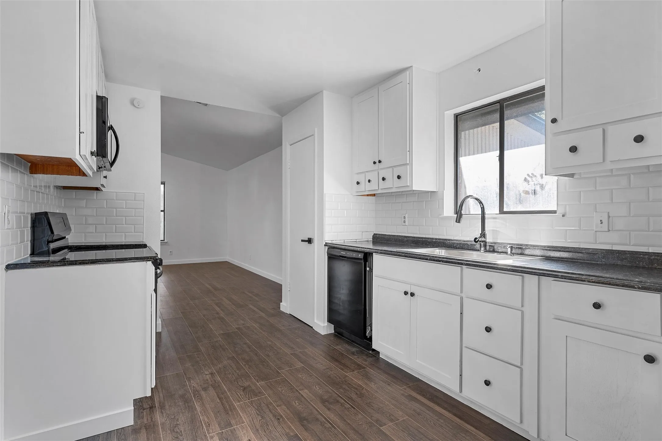 Kitchen featuring tasteful backsplash, white cabinetry, black appliances, and dark wood-style floors