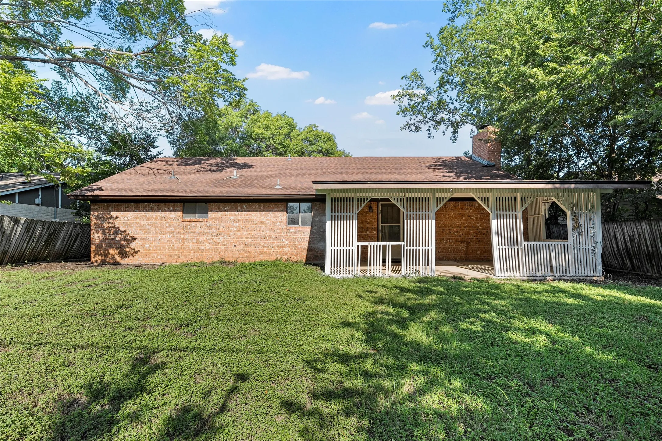 Rear view of property featuring brick siding, a chimney, roof with shingles, and a patio