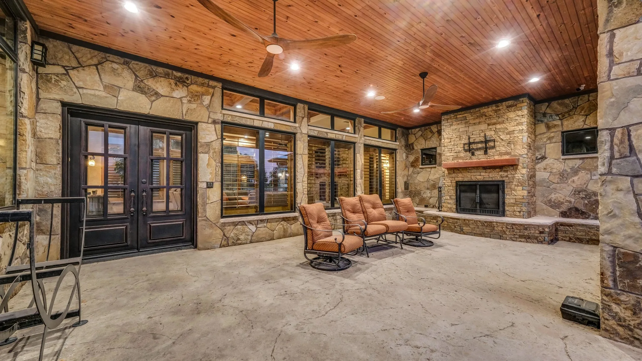 Outdoor living area with stone fireplace, wood ceiling, and multiple seating options for year-round enjoyment.
