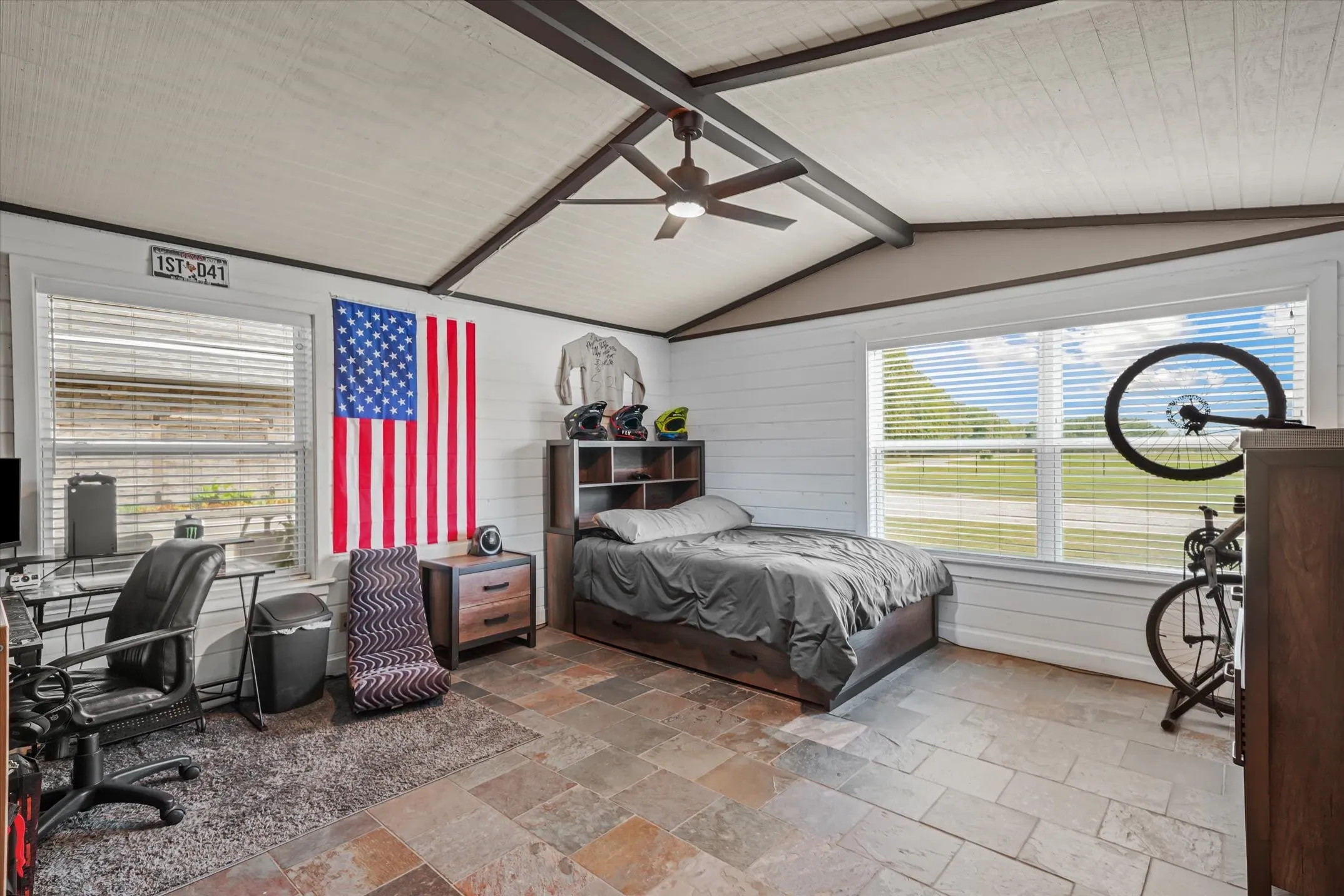 Bedroom featuring a ceiling fan, stone tile floors, an office area, and wooden walls