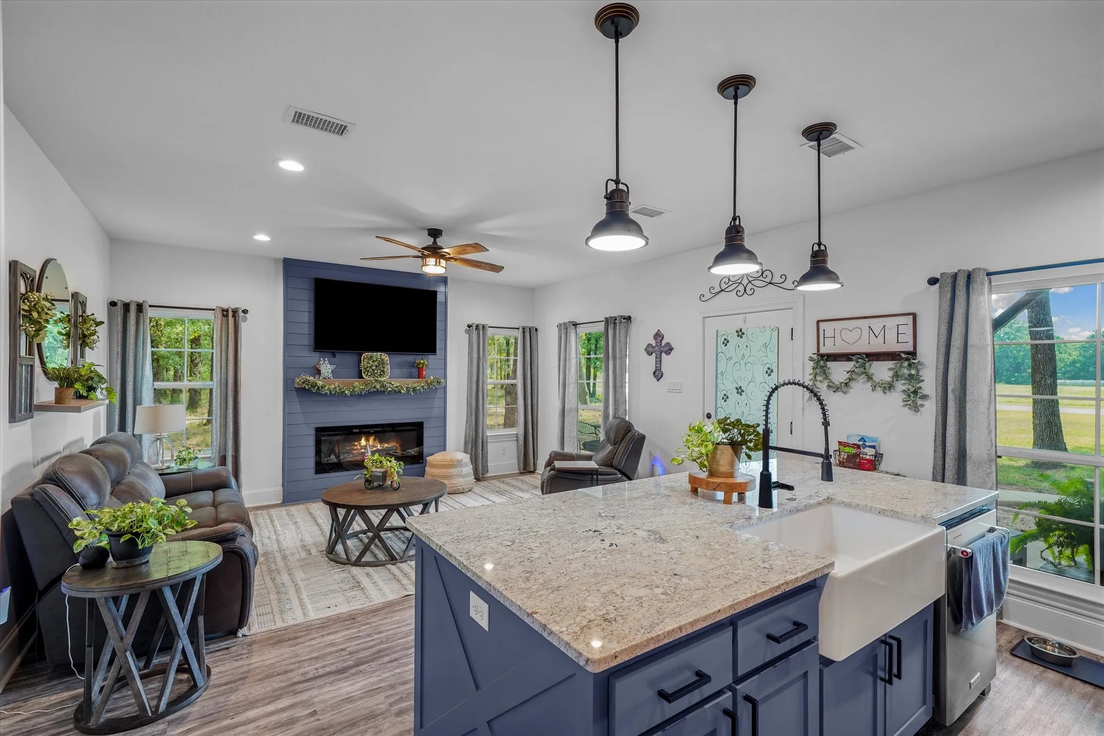 Kitchen featuring blue cabinets, light wood-style floors, pendant lighting, light stone countertops, and a large fireplace