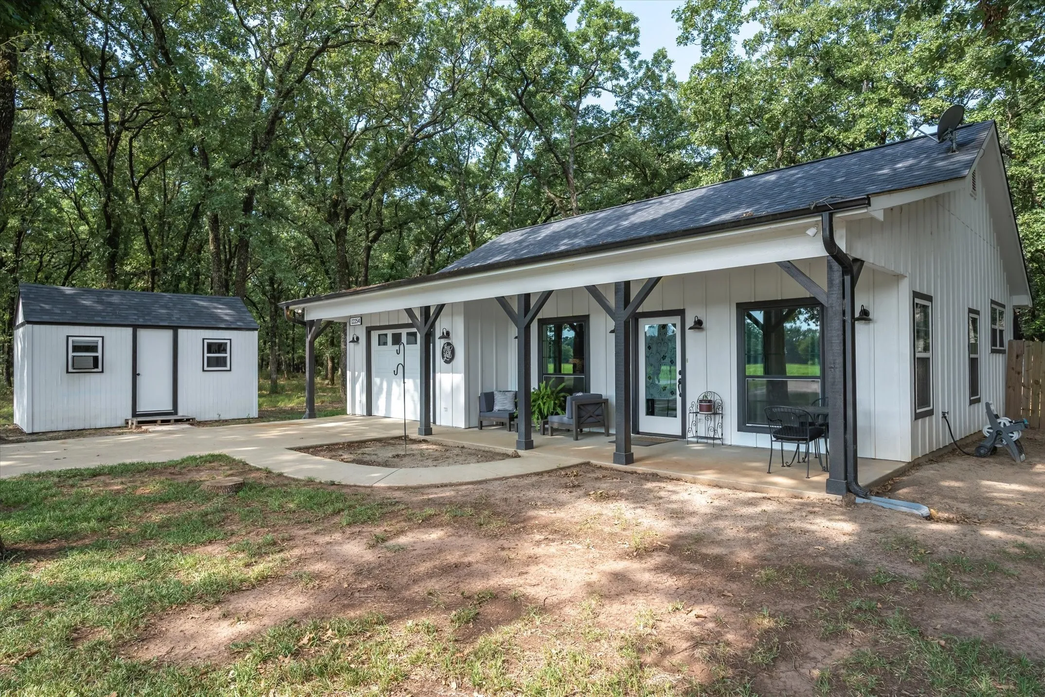 Back of property with covered porch, concrete driveway, roof with shingles, an outbuilding, and a garage