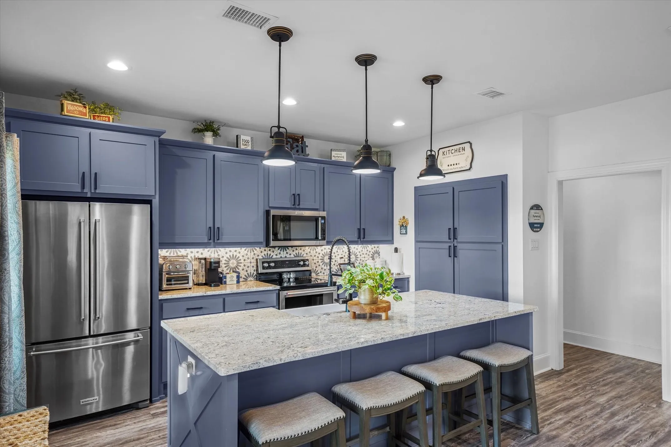 Kitchen with blue cabinets, stainless steel appliances, backsplash, a kitchen bar, and decorative light fixtures