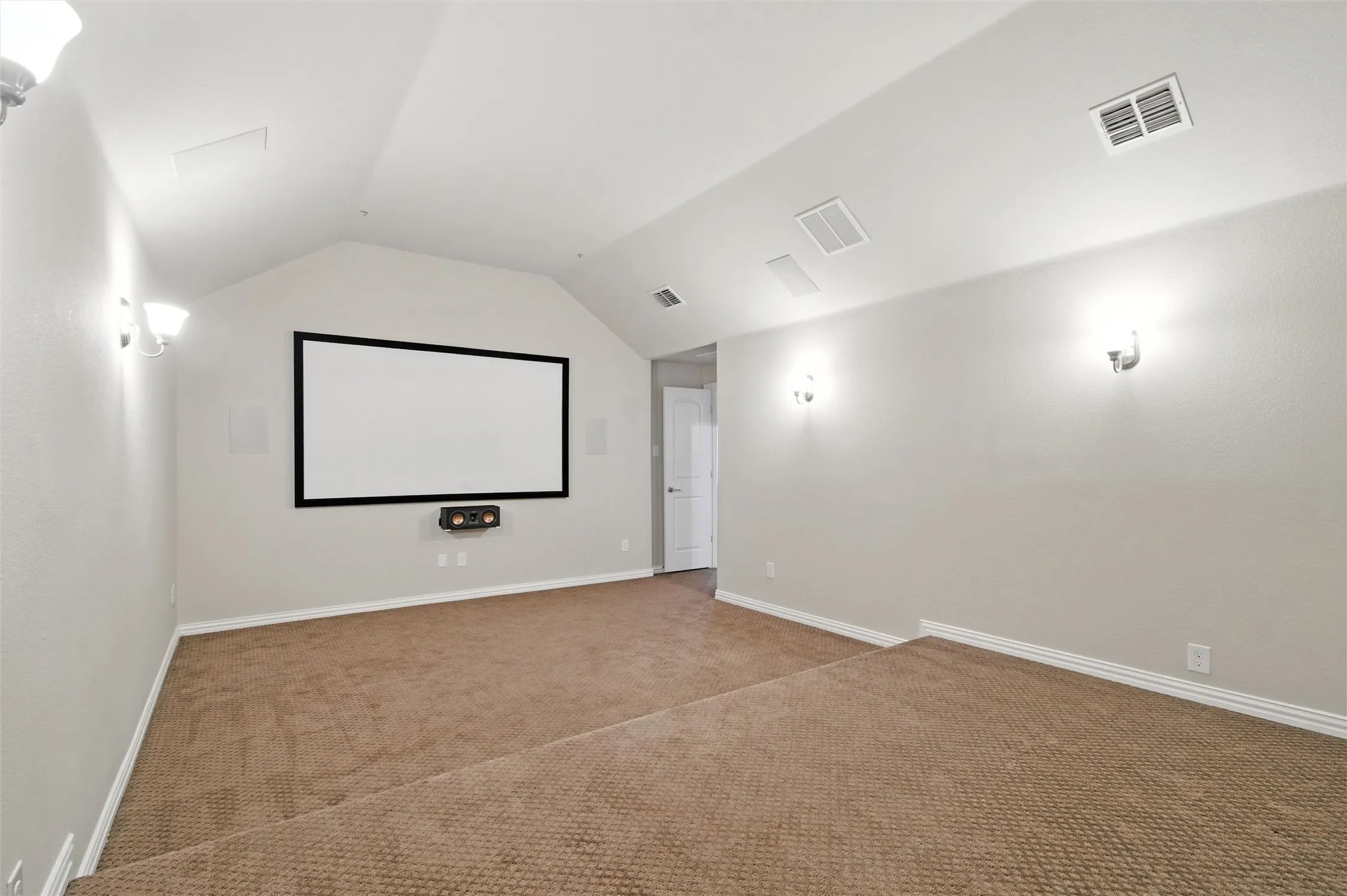 Carpeted home theater room with vaulted ceiling and baseboards